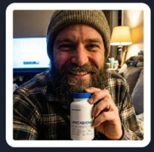 bearded male customer holding DentaBiome oral probiotic supplement bottle indoors and smiling